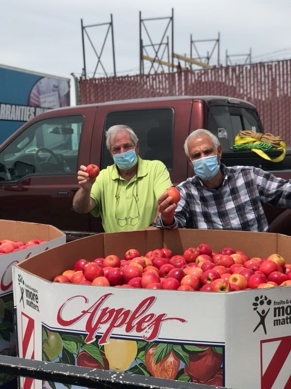 Two elderly men behind a container full of apples 