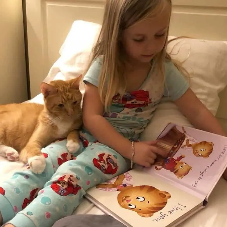 A little girl reading to her orange tabby cat