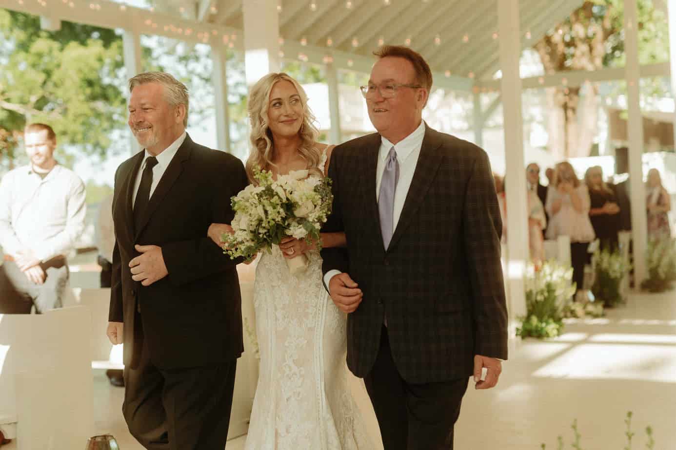 Bride Kelsey Griffith walking down the aisle with her two dads