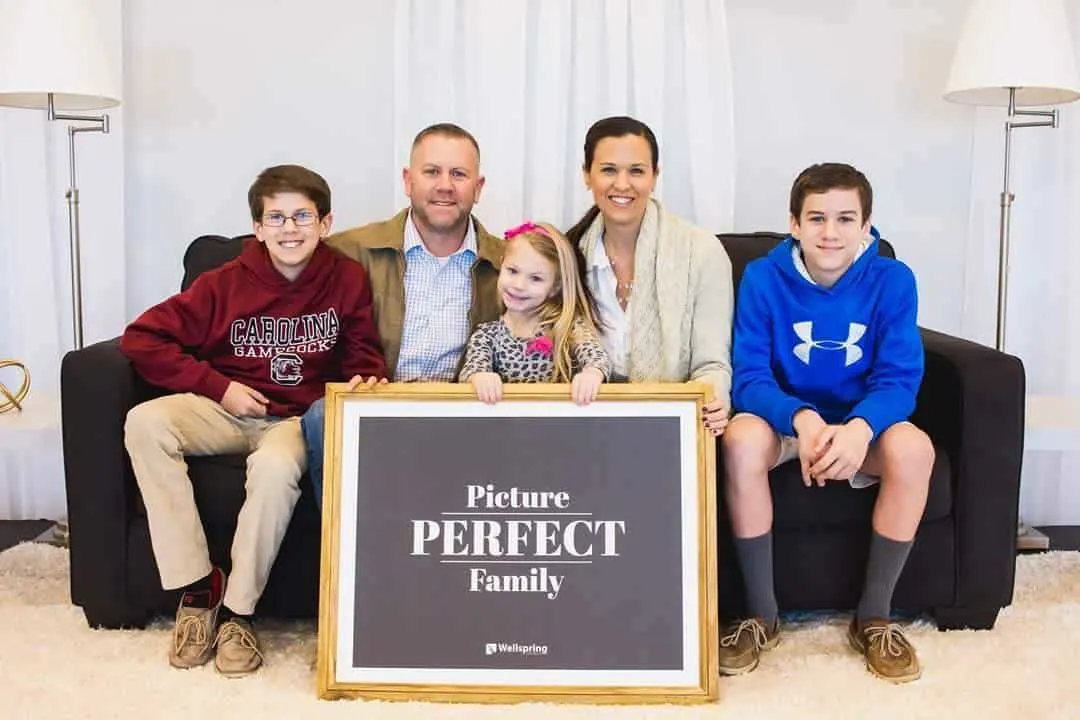 The Hadden family sitting on a black couch posing for a photo with a large frame in front of them that reads "Picture PERFECT Family"