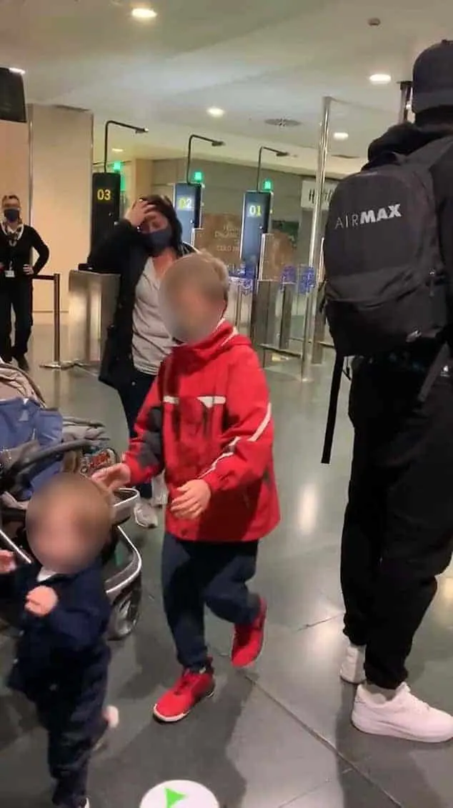A distressed mother in an airport raking her hand through her hair while her two little kids run around