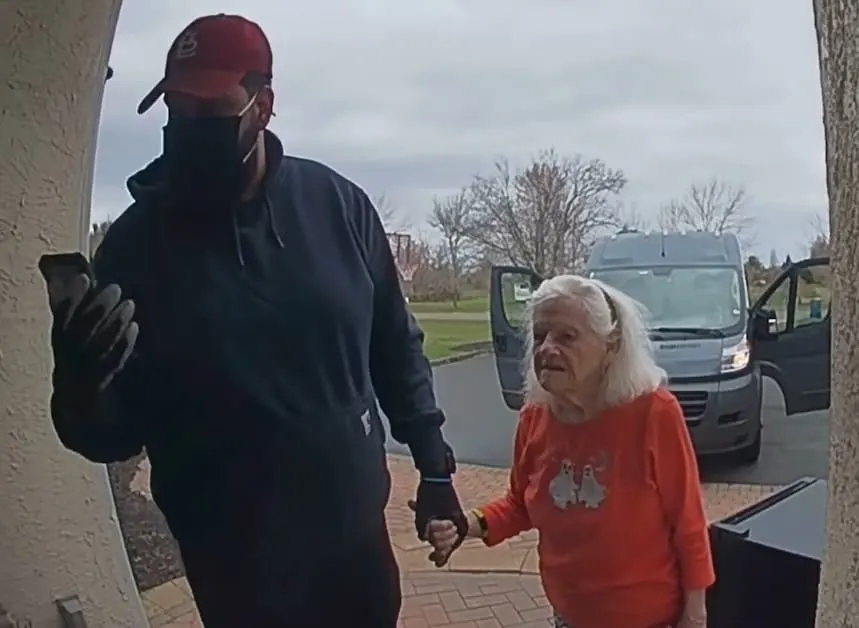 An Amazon delivery driver holding an old woman's hand after ringing the doorbell of her home