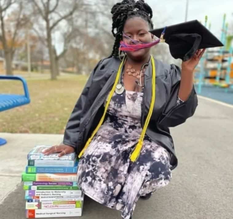 Imunique Triplett touching a pile of books while holding her graduation cap in the other hand