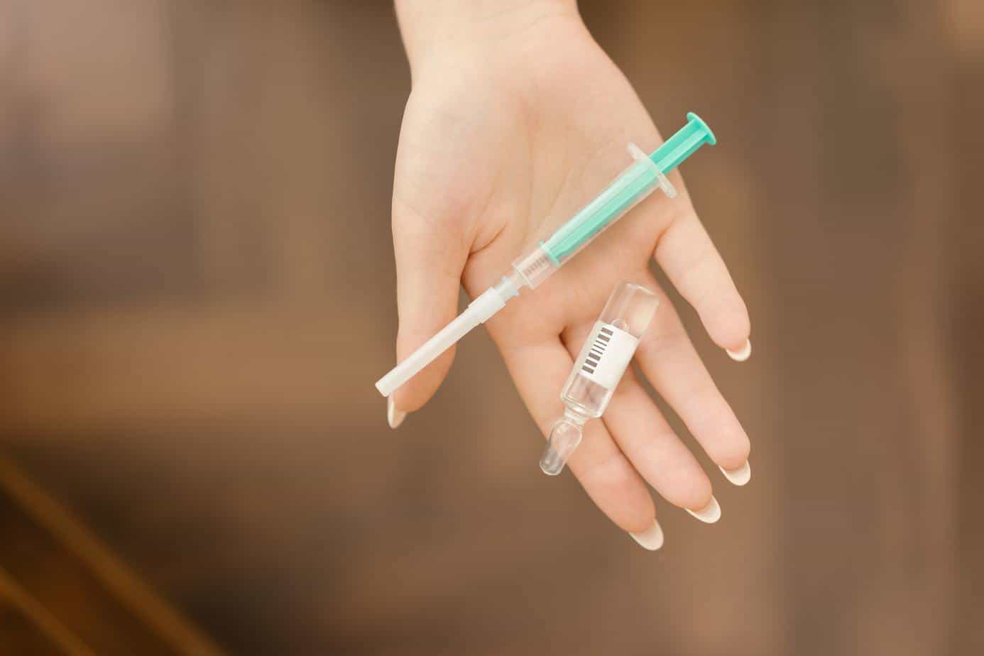 A hand holding an empty vial and a syringe