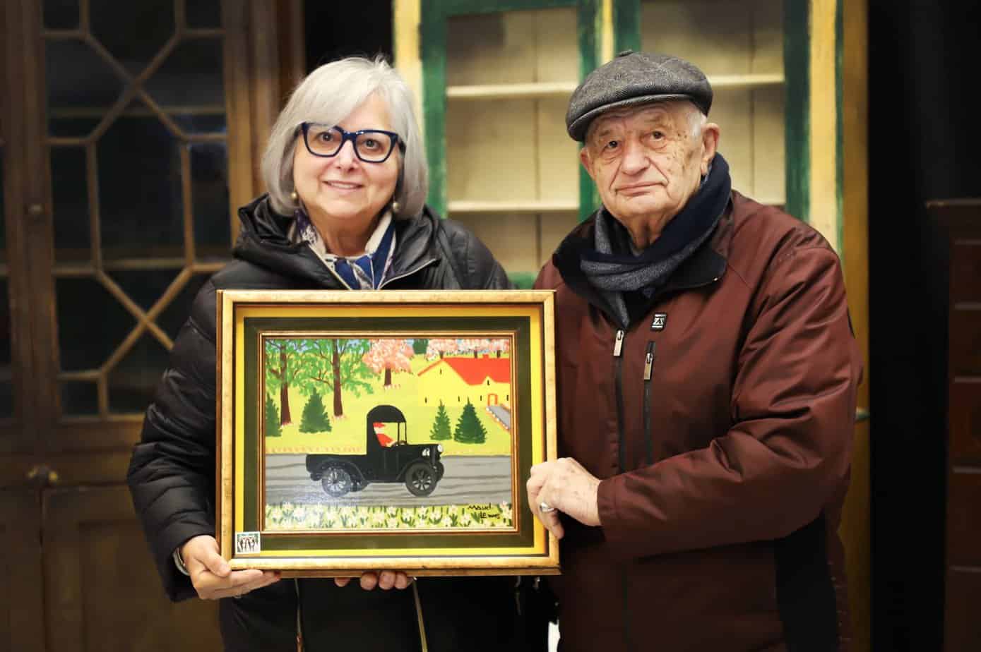 Irene Demas and Tony Demas holding a Maud Lewis painting of a black truck