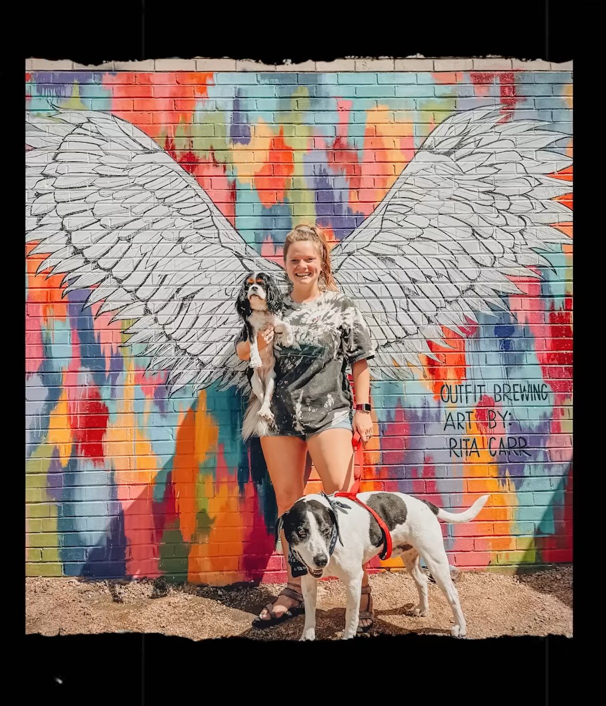 Rita standing in front of her mural along with her dogs.
