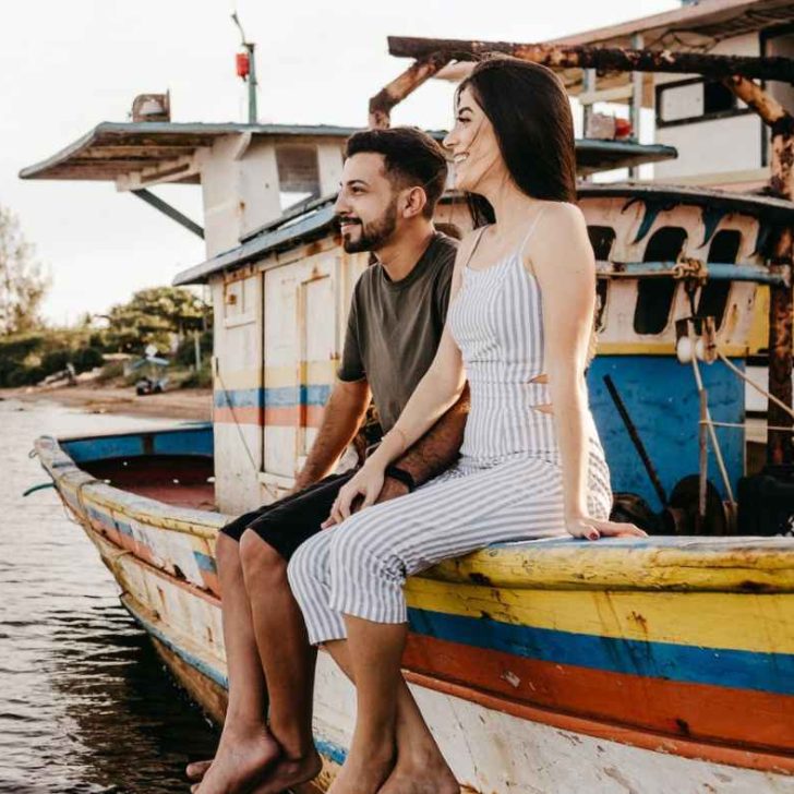 Joyful couple sitting on old boat and holding hands.