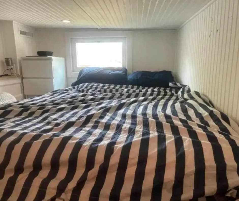 Daniel's bedroom with large, comfy bed with brown and black stripes bed sheet and black pillows, a window and a bedside cabinet.