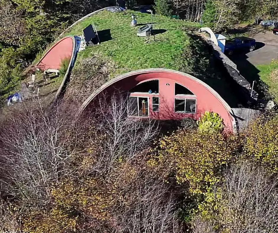 Areal shot of the hobbit home showing tons of earth above it and large glass windows on its wall.