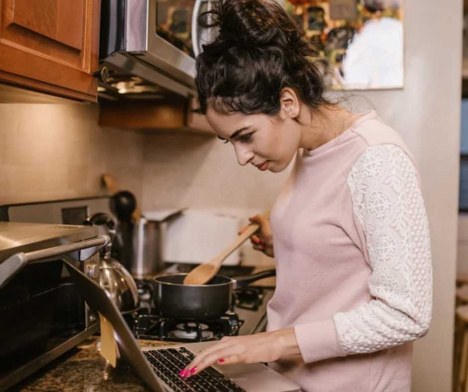 Woman, cooking while working on her laptop