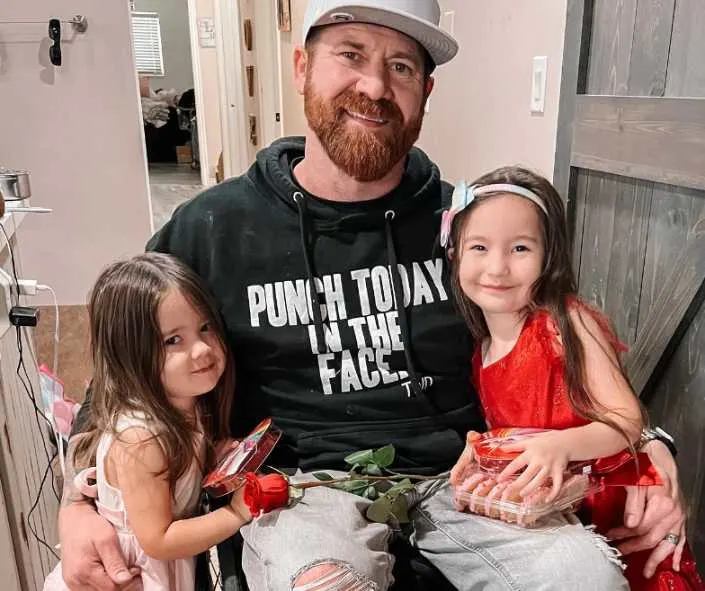 Dan and his daughters posing for a photo while holding flowers and chocolates