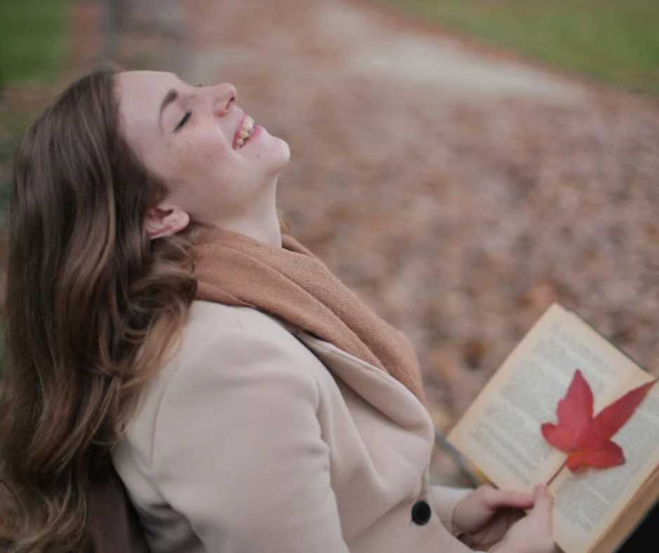 Happy young woman sitting on a bench and holding a book with red leaf