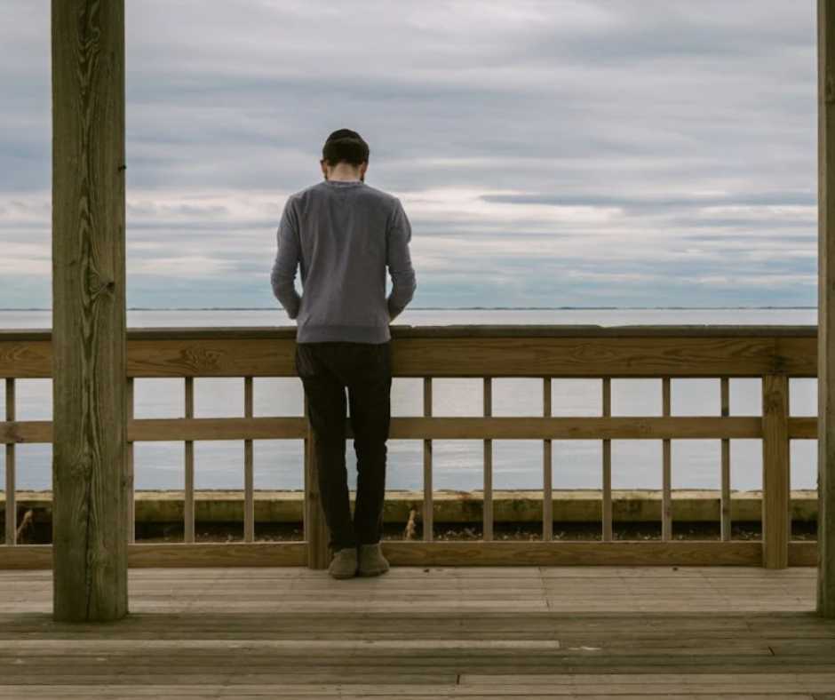 sad man standing by the wooden fence